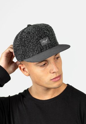 Gray textured cap with a flat brim and a dark gray underside. Features a rectangular branded patch on the front. Worn by a model.