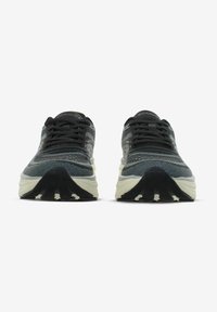 Sneaker neri e grigi con tomaia in rete, punta rotonda, lacci piatti e suola spessa di colore crema. Motivi testurizzati sulla superficie.