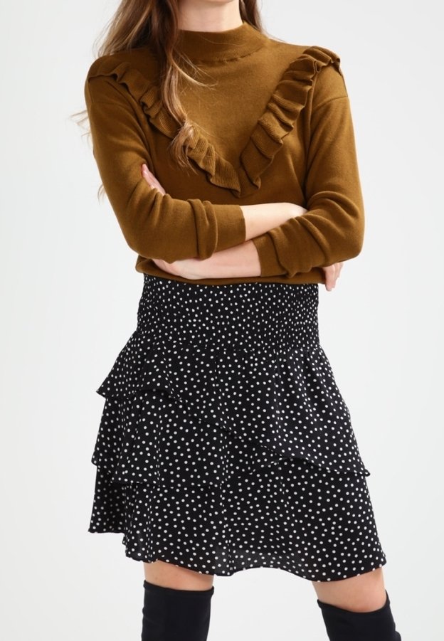 Brauner Pullover mit Rüschendetails am Ausschnitt, kombiniert mit einem schwarzen, gepunkteten, gestuften Rock. Das Outfit hat lange Ärmel und Kniehohe Stiefel.