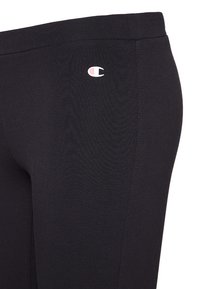 Leggings noirs en coton extensible. Présentent un petit logo blanc et rose sur la cuisse. Texture lisse et design ajusté.
