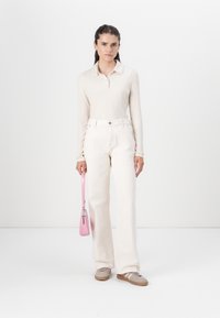 Langermet, ribbet kremfarget polo med lys kremfarget vide jeans. Rosa håndveske med skulderstropp og grå slip-on sko.