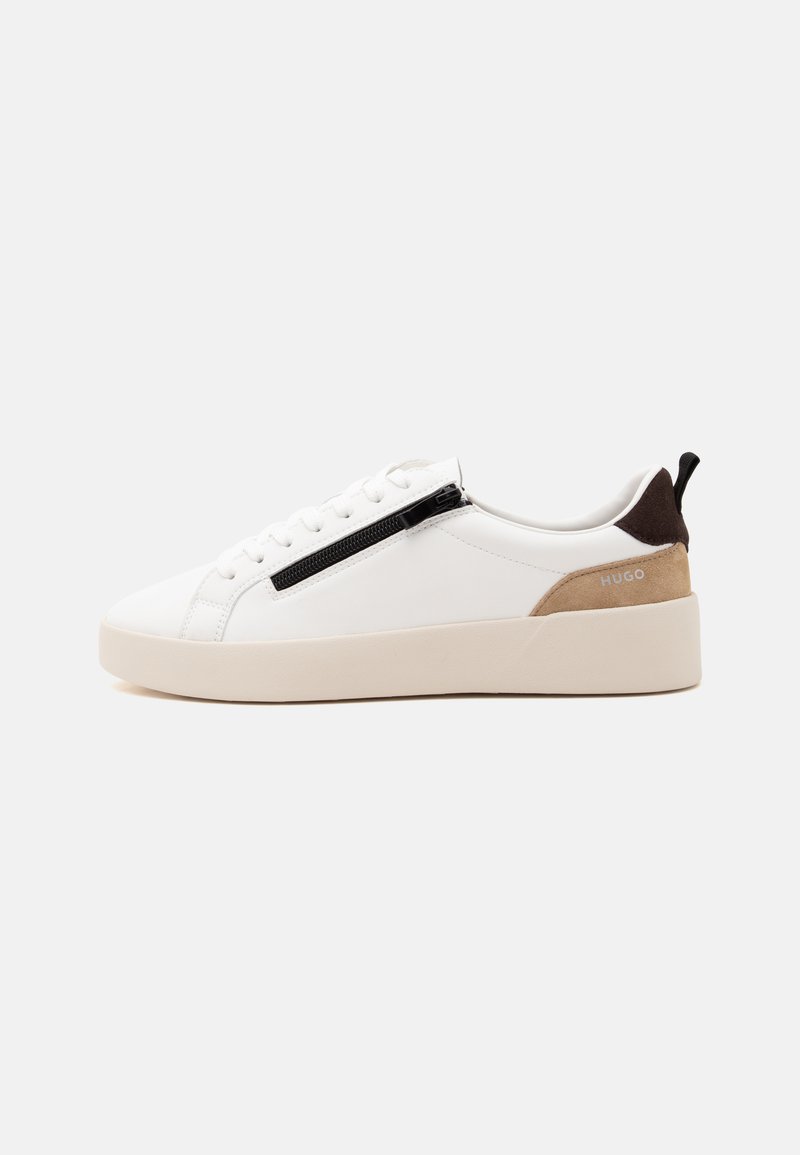 Baskets blanches basses avec semelle beige, fermeture éclair noire sur le côté, partie talon en daim marron clair, languette de talon noire et logo "HUGO".