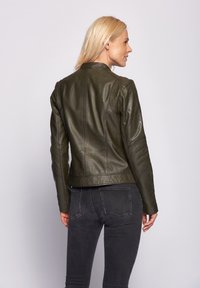 Olivgrön läderjacka med en åtsittande form, dragkedjestängning och detaljerad sömnad. Bärs med mörkgrå jeans som visar en elegant design.