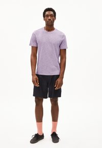 Paarse T-shirt met korte mouwen, zwarte shorts, roze sokken en zwarte schoenen. Het T-shirt heeft een gestructureerde uitstraling; de shorts hebben een eenvoudig ontwerp.
