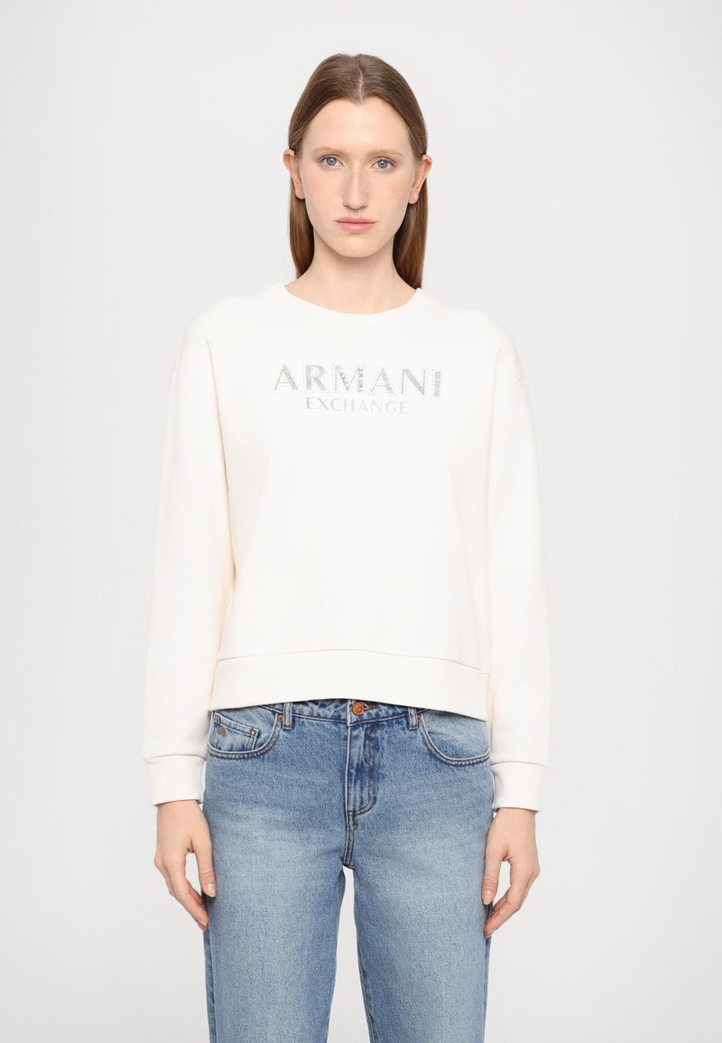 Felpa crema con scollatura tonda, polsini e orlo a costine. Presenta una stampa in glitter argento con la scritta "ARMANI EXCHANGE" sul davanti.