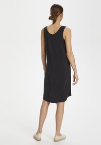 Černé bezrukávové šaty s kulatým výstřihem, volného střihu a hladké tkaniny. Šaty sahají do poloviny stehna a jsou doplněny lehkými botami.