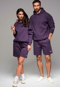 Fioletowe bawełniane bluzy z kapturem i szorty. Bluzy mają sznurki i ściągacze przy mankietach. Szorty charakteryzują się wykończonym dołem i małymi akcentami z logo.