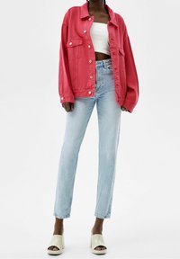 Różowa, oversize'owa kurtka dżinsowa z przednimi kieszeniami, noszona na białym crop topie, zestawiona z jasnoniebieskimi spodniami prostymi i beżowymi butami na platformie.