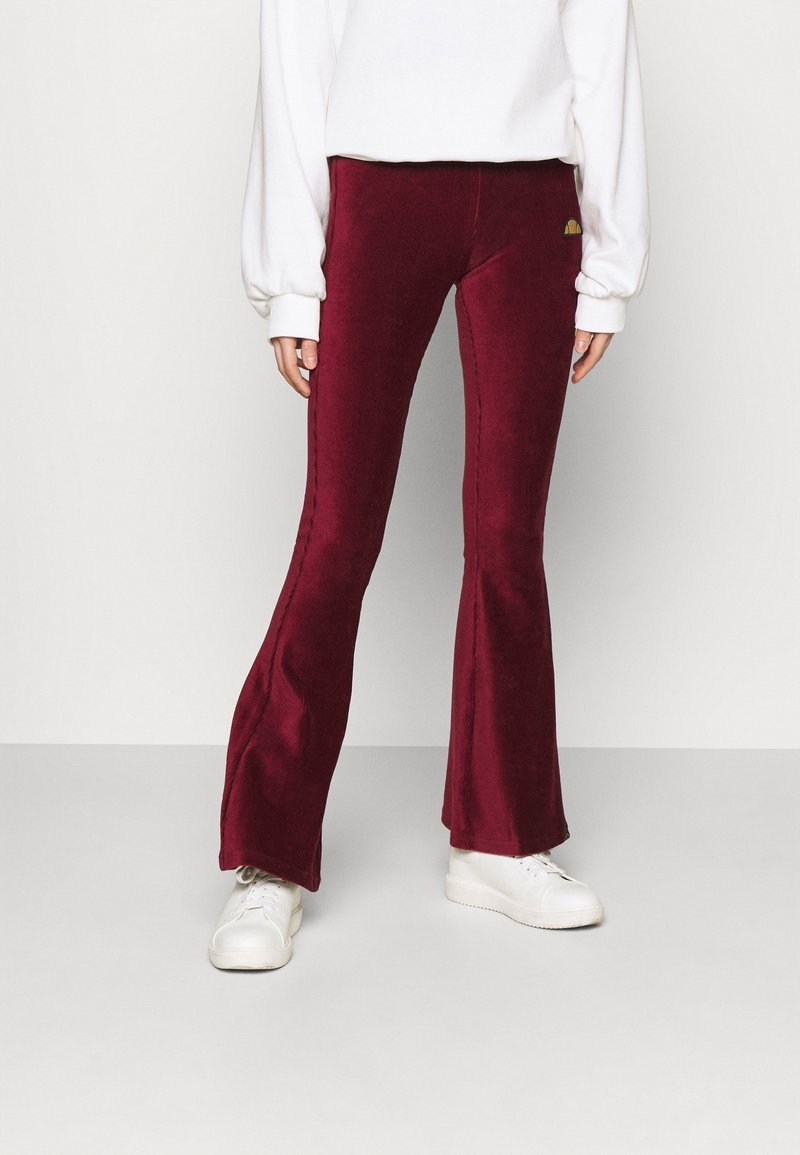Burgundy kordfløyelsbukser med bredere ben och mid-rise midja, med sid sömmar och en liten logotypdetalj, åtföljd av vita sneakers och en vit topp.