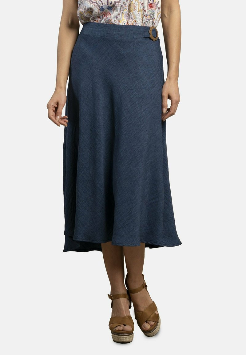 Una falda de línea A hasta la rodilla en un tejido azul oscuro texturizado, con un detalle de botón lateral y un dobladillo ligeramente acampanado. Combinada con sandalias de cuña color marrón claro.
