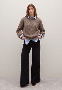 Bruine gestructureerde breisweater over een lichtblauw blousehemd, gecombineerd met zwarte wijde broek en bruine haklaarzen. Eenvoudige en gelaagde look.