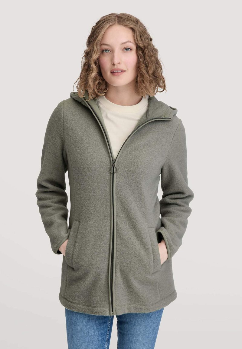 Olivgrüne Fleecejacke mit Kapuze, durchgehendem Reißverschluss und Seitentaschen. Weiche Textur und taillierte Passform, kombiniert mit einem hellen Shirt darunter.