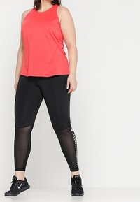 Top atletico rosso senza maniche abbinato a leggings neri con pannelli in rete e accenti bianchi, progettato per un comfort e un movimento ottimali.