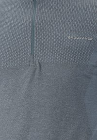 Grå atletisk top med en kvart lynlås, tekstureret mønstret stof i den øvre sektion og glat nederste sektion. Har "ENDURANCE" logo.