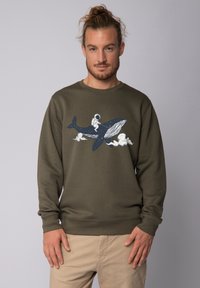 Dunkelolivgrüner Pullover mit langen Ärmeln, der ein weißes und dunkelblaues Grafikdesign eines Astronauten zeigt, der auf einem Wal zwischen Wolken reitet.
