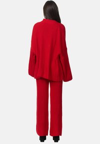 Completo a due pezzi lavorato a maglia rossa, caratterizzato da un maglione oversize e pantaloni dritti con texture a costine.