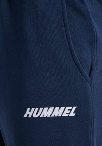 Navyblaue Sweatpants aus weichem Stoff, mit einer Seitentasche und einem auffälligen weißen "HUMMEL"-Logo nahe dem Saum.