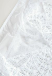 Balts mežģīņu apakšveļas komplekts ar sarežģītiem rakstiem, caurspīdīgiem tīkliņiem un mīkstām tekstūrām. Malās ir izsmalcināti izšuvumi, kas uzlabo dizainu.