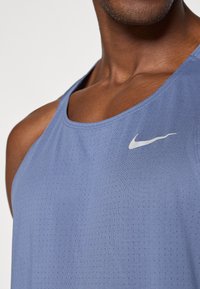 Débardeur sans manches Nike bleu clair en tissu respirant avec de petits perforations, arborant un logo blanc discret sur la poitrine.