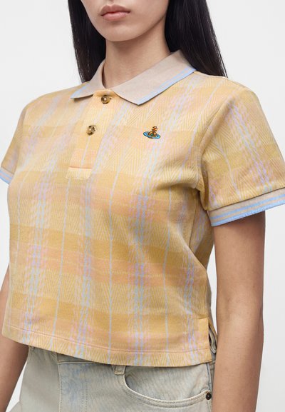 Femme portant un polo à manches courtes jaune à carreaux avec un bord bleu et un petit logo brodé sur la poitrine.