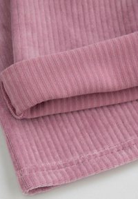 Różowy, żeberkowany materiał o miękkiej fakturze, z delikatnymi liniami i złożonym brzegiem. Tkanina ma przytulny, zachęcający wygląd.