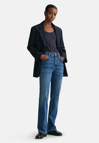 Marineblazer over en tætsiddende mørk tanktop, parret med lyseblå lige jeans og sorte sko. Denim har en glat tekstur; enkel design.