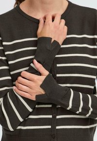 Stripet cardigan i mørk brun og hvit. Strikkemateriale, med lange ermer som har tommelhull og knappeåpninger foran.