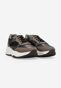 Un par de zapatillas negras y marrones con cordones y suelas gruesas blancas, mostradas desde un ángulo frontal sobre un fondo blanco.