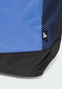 Bolso azul con una superficie de tela lisa, que presenta un acento de malla negra y una base negra. Incluye una pequeña etiqueta con el logo en la esquina.