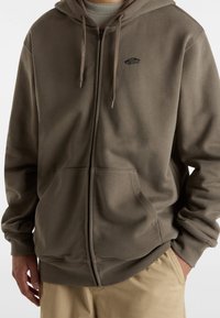 Oliwkowa bluza z zamkiem błyskawicznym, z przednią kieszenią, z małym czarnym logo na klatce piersiowej. Miękka tkanina, luźny krój i kaptur ze sznurkiem.