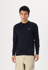 Μπλέ ναυτικού μακρυμάνικη μπλούζα από πλεκτό ύφασμα, με στρογγυλή λαιμόκοψη και μικρό λογότυπο στο στήθος. Απαλή υφή, εφαρμοστή σχεδίαση.