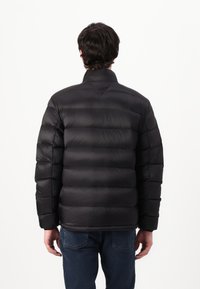 Svart pufferjakke med høy krage, med horisontale sømmer for isolasjon. Bakfra viser den en jevn tekstur og en tettsittende design.