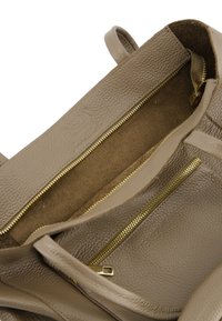 Beige leren handtasinterieur met zowel gladde als textuurafwerkingen, voorzien van twee goudkleurige ritsen en een zachte, suede-achtige voering.