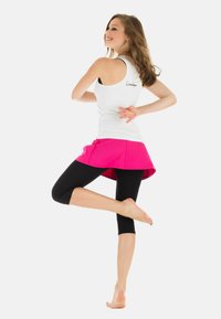 Weißes Tanktop, rosa Rock und schwarze Capri-Leggings. Das Tanktop hat ein Racerback-Design, und der Rock hat einen ausgestellten Saum mit einem schichtigen Look.
