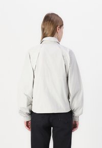 Hellgraue Jacke mit strukturiertem Kragen, elastischen Bündchen und lockerer Passform, aus einem glatten, leichten Material gefertigt.