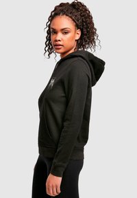 Black pullover hoodie featuring a front pocket, drawstring hood, and a graphic print on the chest. Soft fabric with ribbed cuffs.