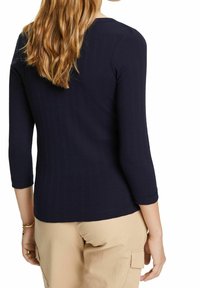 Mörkblå ribbad långärmad topp med rund halsringning och trekvartslånga ärmar, sedd bakifrån mot en neutral bakgrund.