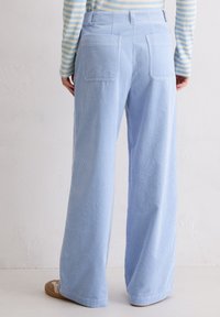 Hellblaue Cordhosen mit weitem Bein und vertikalen Streifen, ausgestattet mit zwei Gesäßtaschen und einem glatten Bund, kombiniert mit beigen Schuhen.