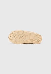 Semelle de sneaker beige clair en caoutchouc texturé, avec un motif de crampons pour une meilleure adhérence. La base est plate et durable, conçue pour la stabilité.