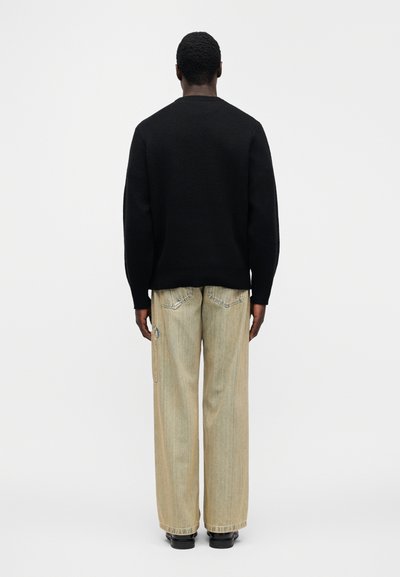 Μαύρο πλεκτό πουλόβερ με στρογγυλή λαιμόκοψη, συνδυασμένο με ανοιχτό μπεζ παντελόνι με φαρδ ιά πόδια, που έχει πίσω τσέπες και πλευρικό φερμουάρ.