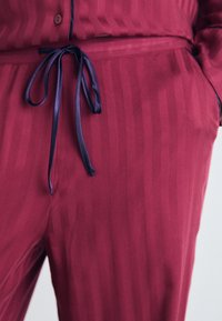 Burgundy loungewear-set med randig textur; midjeband med en mörk satinslips. Slät tyg med subtil lyster.