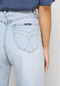Jeans de ganga azul claro com cintura alta e um bolso traseiro com um design curvo distinto e um rótulo preto "ROLLAS".
