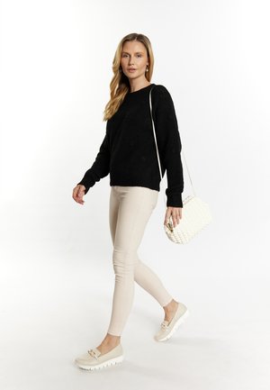 Mustat neulepusero, jossa on tekstuurisia kukka-yksityiskohtia, beige slim-fit-housut ja kerma-valkoinen olkalaukku. Vaaleat kengät, joissa on nauha-yksityiskohta.