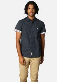 Korte mouw shirt in marineblauw met een gestructureerd patroon, witte bloemenmanchetten en een borstzak. Beschikt over een knoopsluiting aan de voorkant en een label.