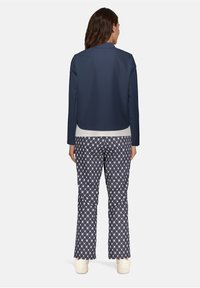 Veste bleu marine courte avec une texture lisse, associée à un pantalon à motifs en bleu foncé et blanc en formes de losange, complété par des chaussures légères.