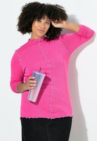 Vaaleanpunainen pitkähihaisen paita, jossa on aaltoileva helma ja ompelu-yksityiskohdat, yhdistettynä kirkkaaseen, helmiäishohtoiseen juomamukiin. Tausta on yksivärinen valkoinen.