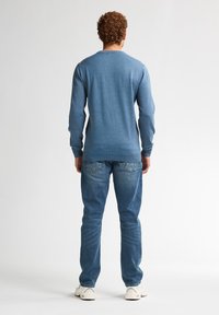 Blauwe trui met lange mouwen en een ronde hals, gecombineerd met blauwe jeans. De stof lijkt glad en gestructureerd, met een getailleerd ontwerp.