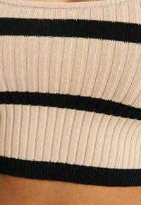 Gerippter, verkürzter Pullover mit alternierenden beigen und schwarzen horizontalen Streifen. Hergestellt aus weichem Strickmaterial mit einem dicken, strukturierten Band am unteren Rand.