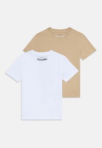 Two t-shirts are shown: one white and one beige. Both have short sleeves, crew necks, and feature "Calvin Klein" branding on the neck.