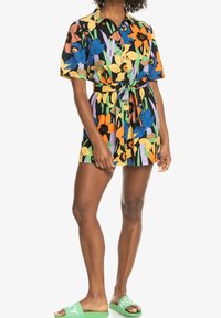 Blomstrande mönstrad kortärmad klänning i svart med flerfärgade accenter; midja med bälte; lättviktsmaterial; matchad med gröna sandaler.